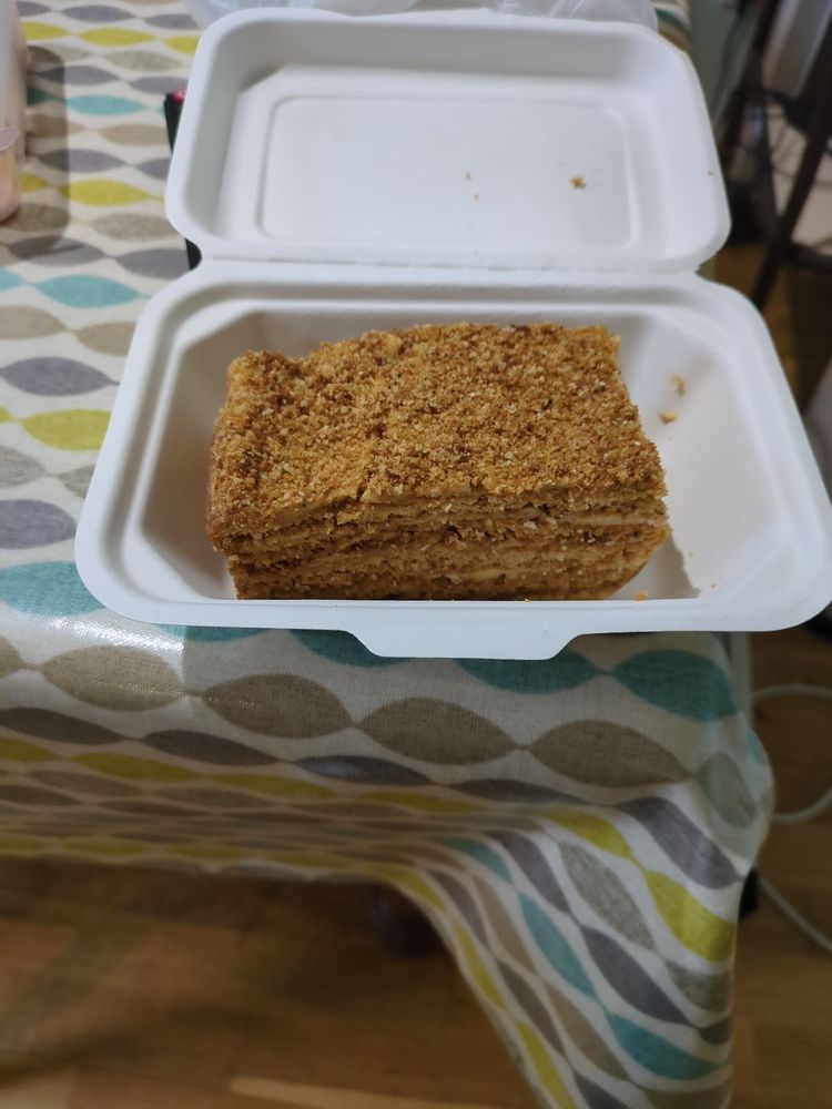 A large square slice of honey cake in an open takeaway box on a patterned tablecloth